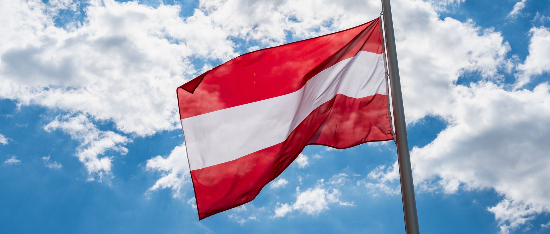 Flagge Österreichs vor blauem Himmel mit leichten Wolken